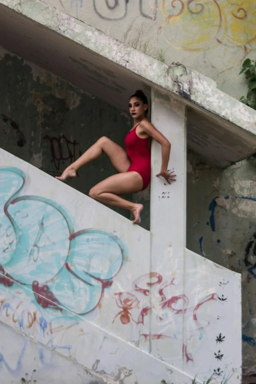 a woman in a red swimsuit and red shoes is leaning on a graffiti wall while on the edge