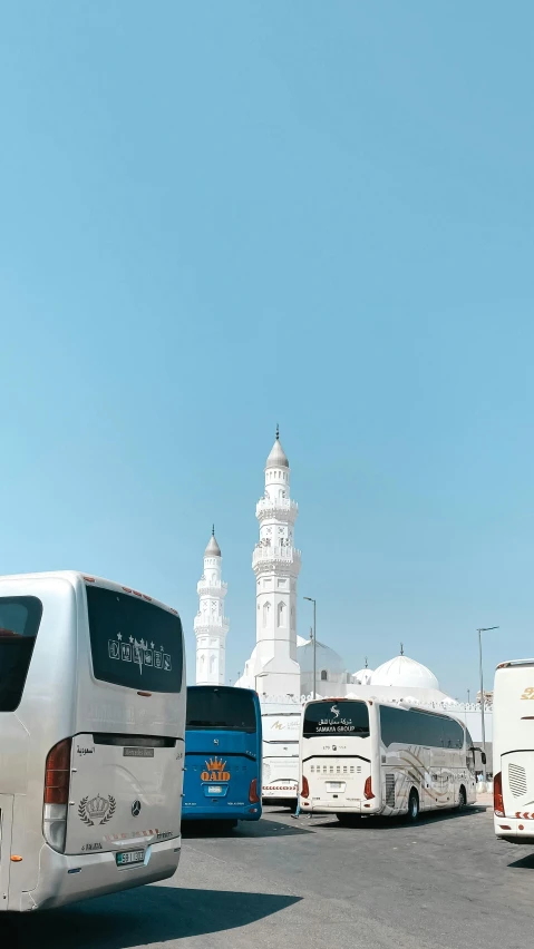 many buses parked on the pavement near a tower