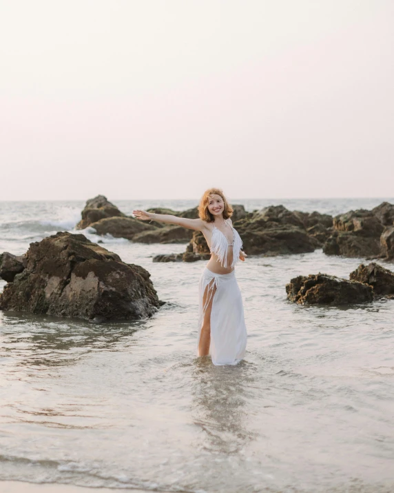 a woman wearing white in the water next to some rocks