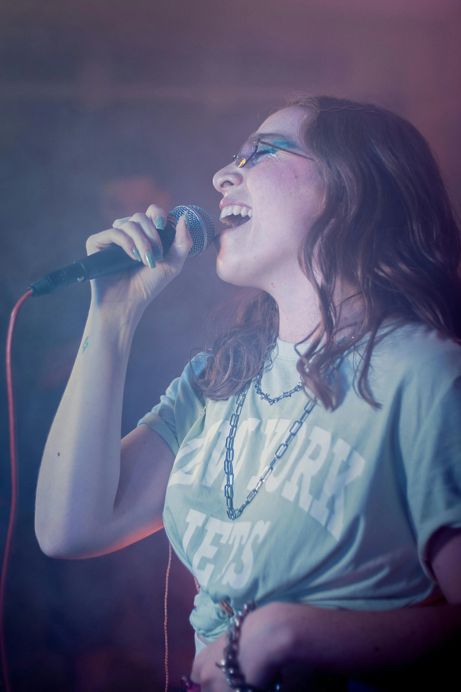 a woman is singing with a microphone and holding a necklace