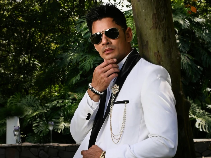 a man in white blazer and sunglasses standing next to tree