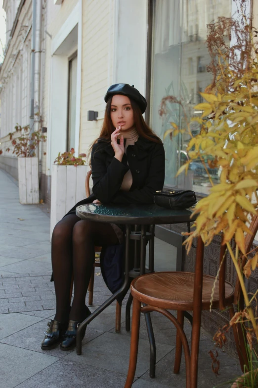 a young lady sitting at a small table, smoking a cigarette