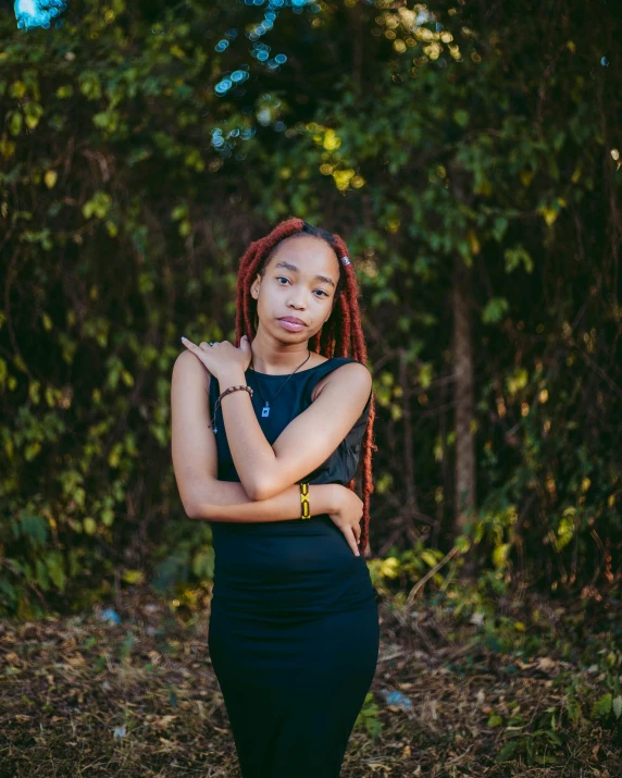 a woman with red dreadlocks stands in the woods