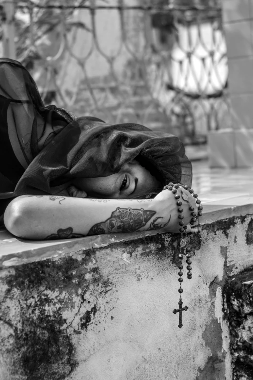 a woman laying on a ledge with her head under a blanket