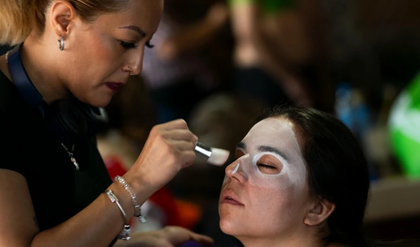 a woman with white mask applying eyeliner on her