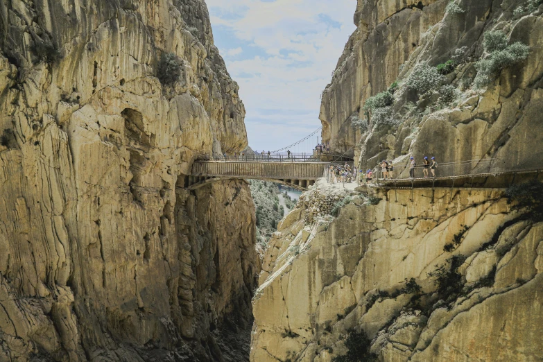 people walking across a narrow bridge between two rocky cliffs