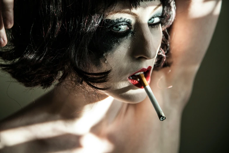 a woman with makeup painted white smokes a cigarette