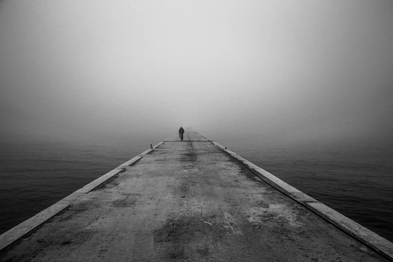 a man standing at the end of a pier in the fog