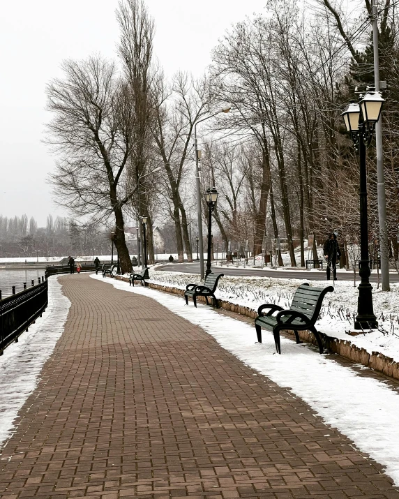 a sidewalk next to a park filled with snow covered benches