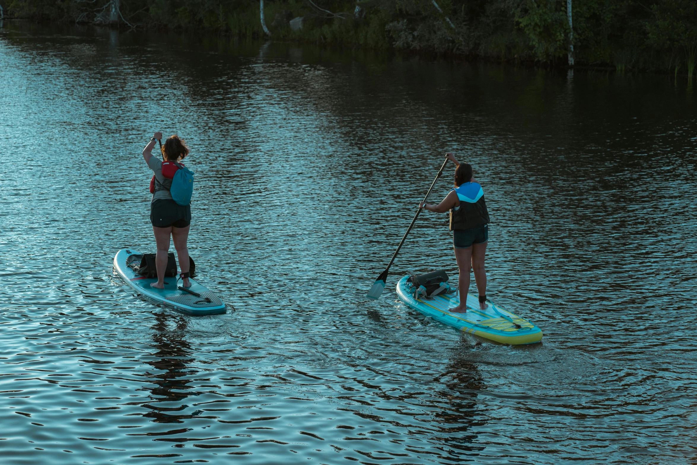 two young women paddle board through the water