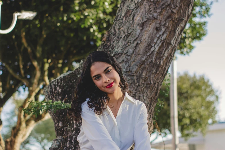 a woman in white poses for the camera beside a tree