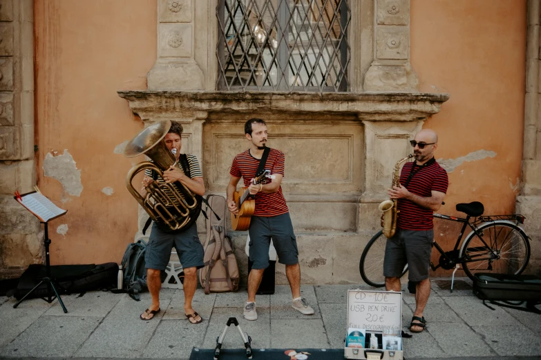 three guys with musical instruments in front of a building