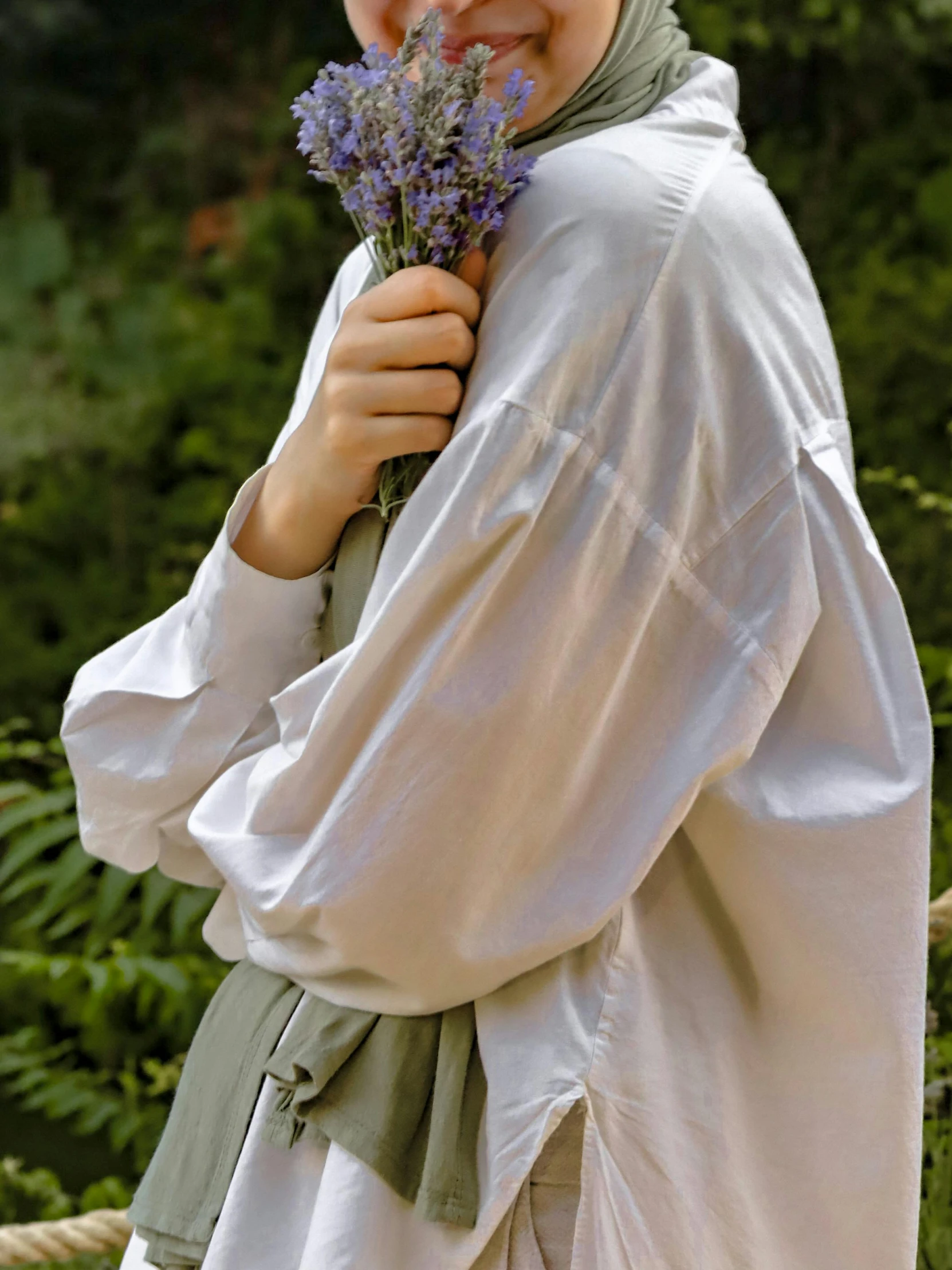 a woman standing holding a bunch of purple flowers