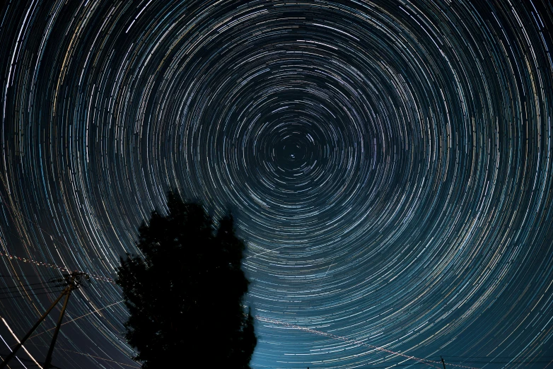 night sky with stars moving over a tree