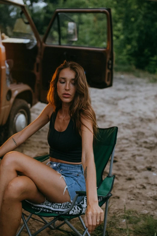 a pretty young woman sitting in a camping chair in front of a truck