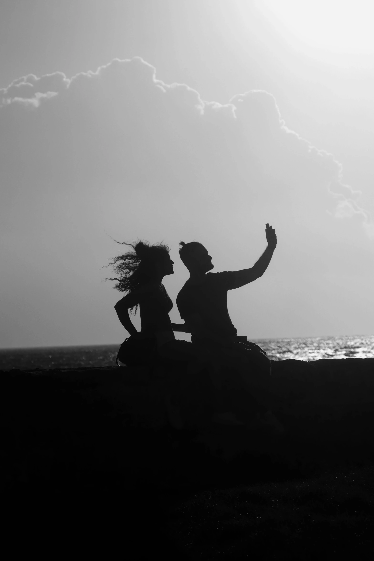 two people are sitting on the beach facing the ocean