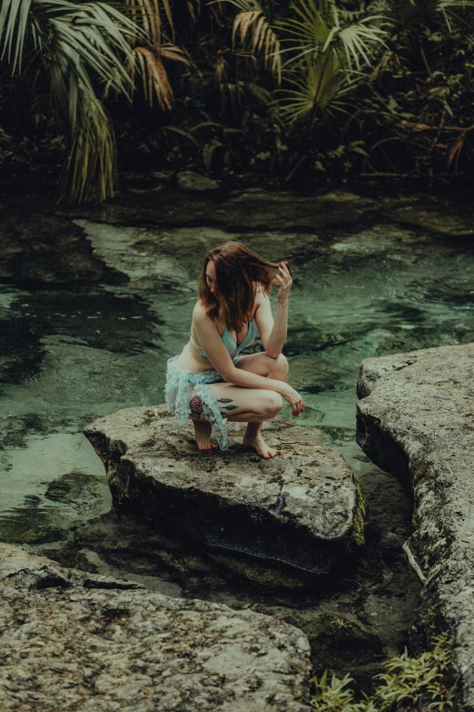 a woman is sitting on a rock next to a stream