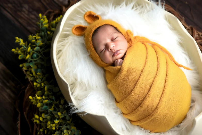 the baby in the yellow bear outfit is asleep on a white cloth