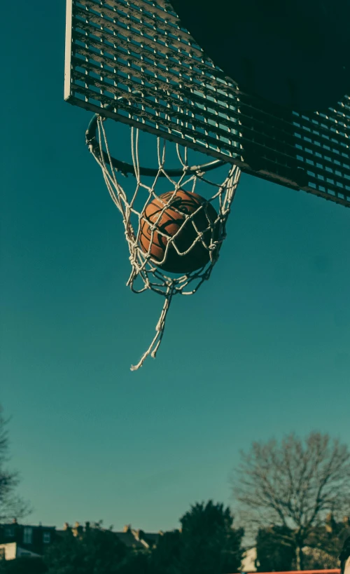 an orange basketball is in the net being suspended by someone