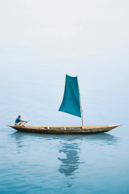 a man is sitting in the ocean on a long boat with a sail