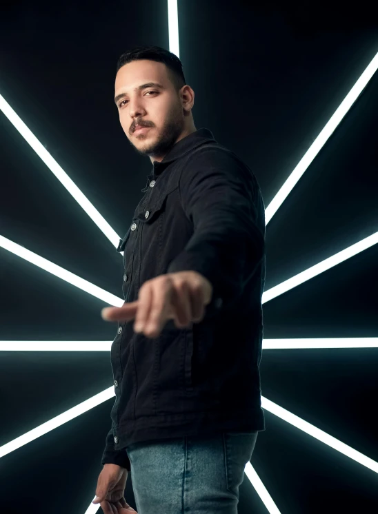 a man in a black jacket stands by a bright, reflective, backdrop