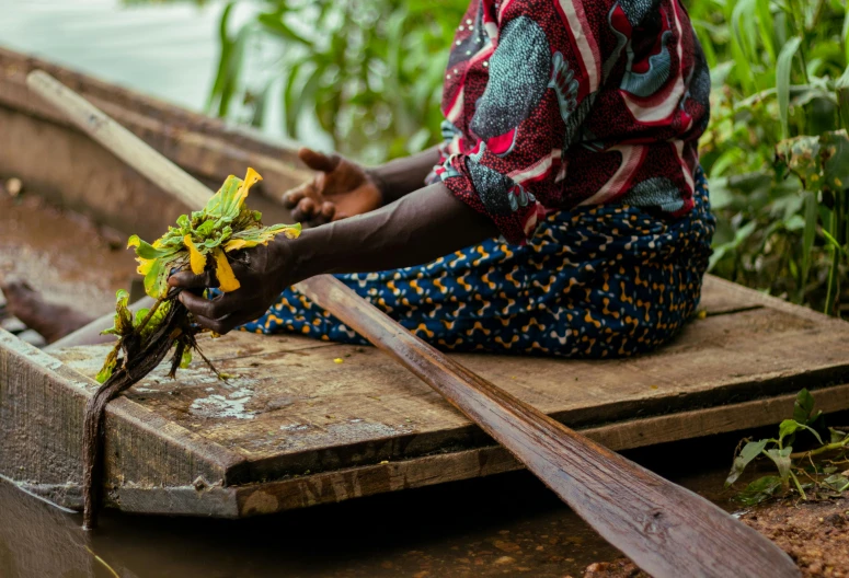 a woman sits on a boat with green leaves on her fingers