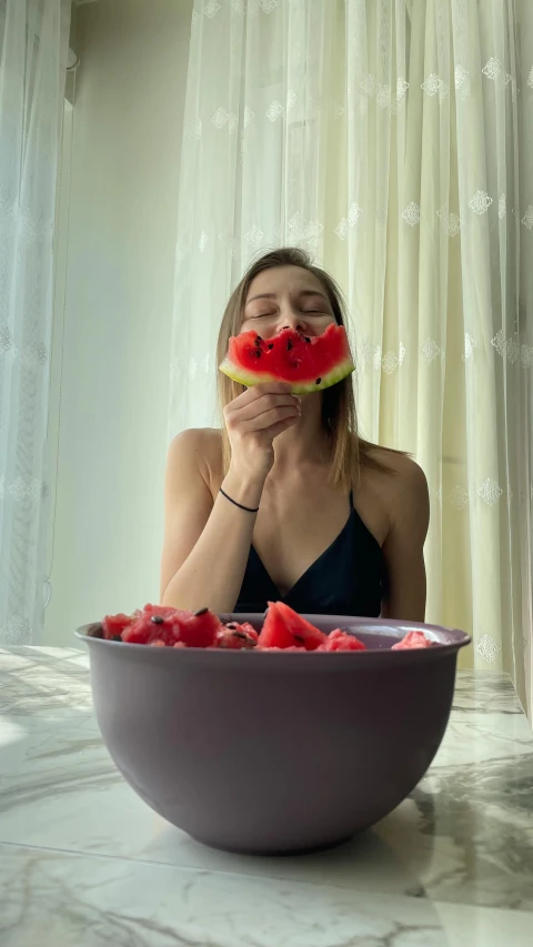 there is a young lady holding her face with a slice of watermelon in front of her mouth