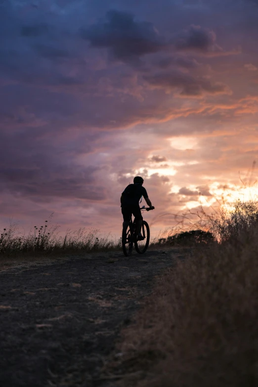 person riding bike on hill at sunset with clouds