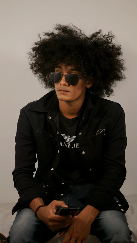 a black man with curly hair and sun glasses sitting down