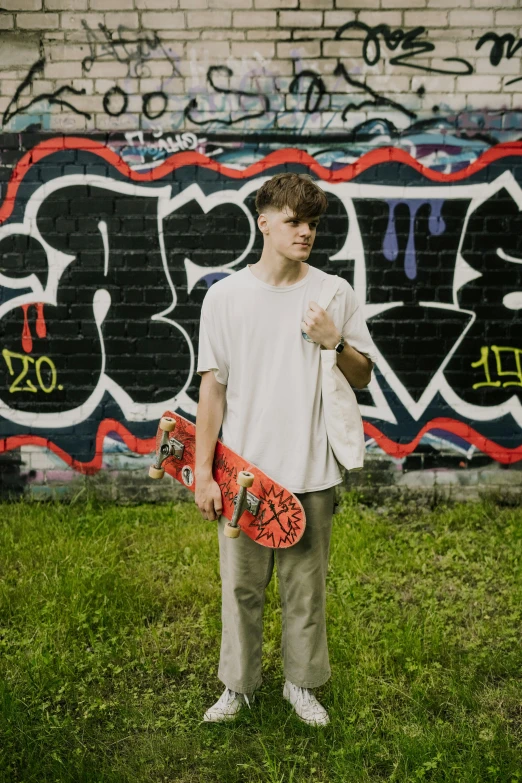 a man holding a skateboard in front of a wall covered with graffiti