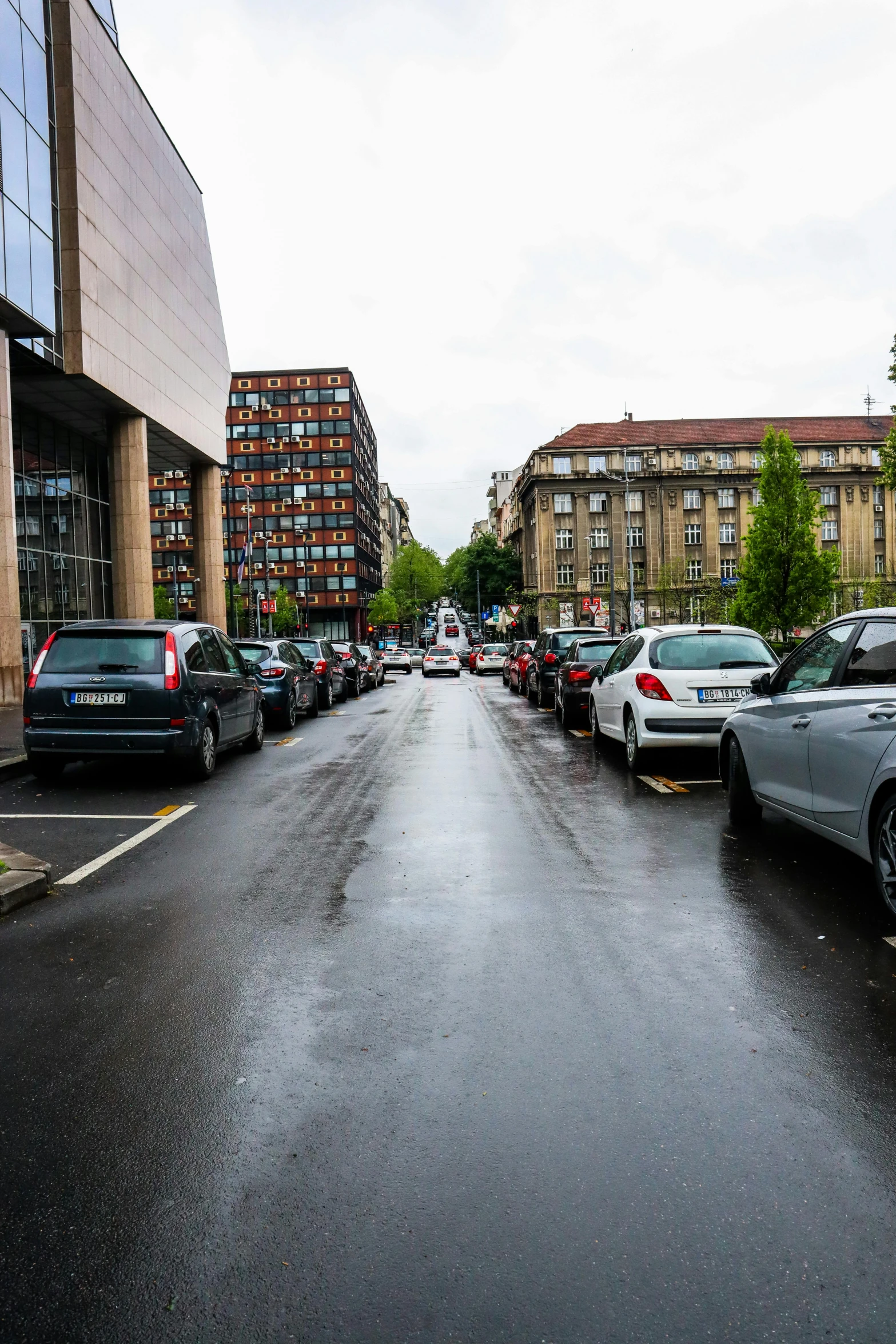 a wet city street is lined with parked cars