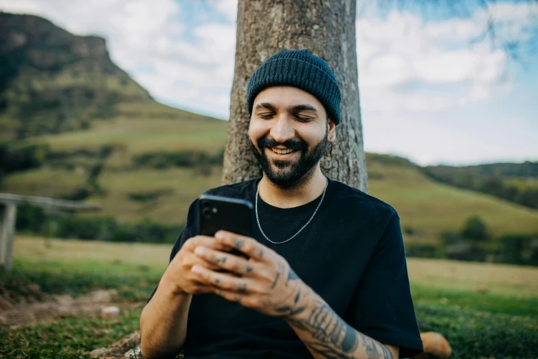 the young man is sitting in the grass looking at his cellphone