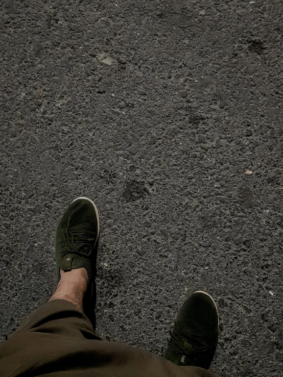 feet in brown pants and green shoes standing on asphalt