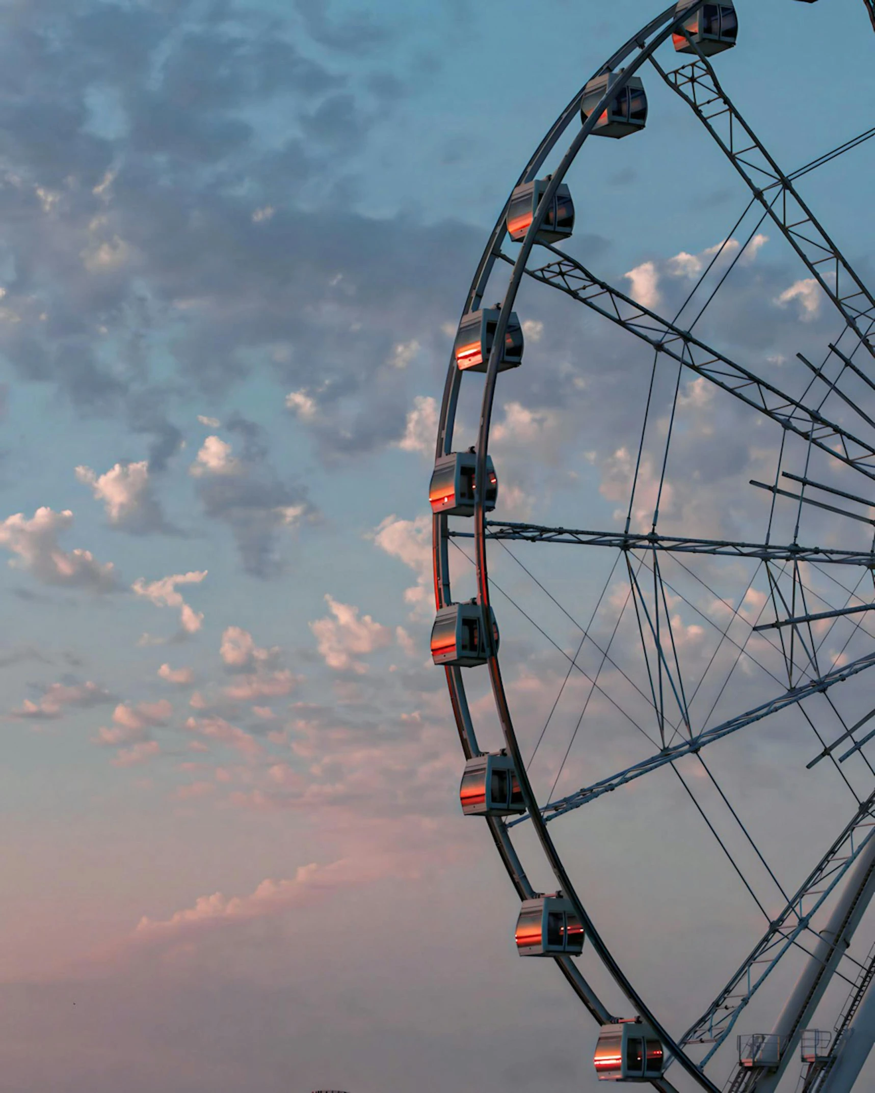 a ferris wheel sits under the blue cloudy sky