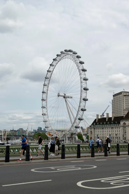 some people are standing by a fence in front of a ferris wheel