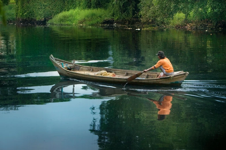 man in a rowboat on calm waters with trees around