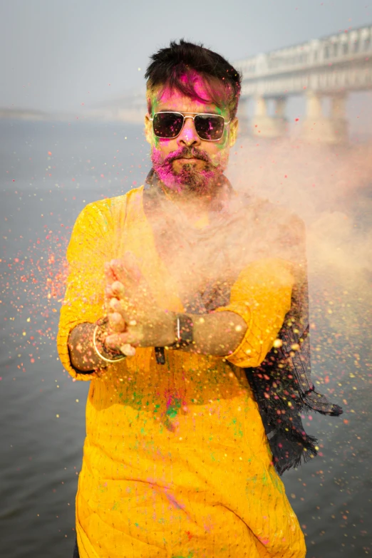 man dressed in yellow holding a cellphone while sprinkles colored powder around him