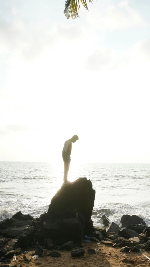 a man on top of a rock looking out at the ocean