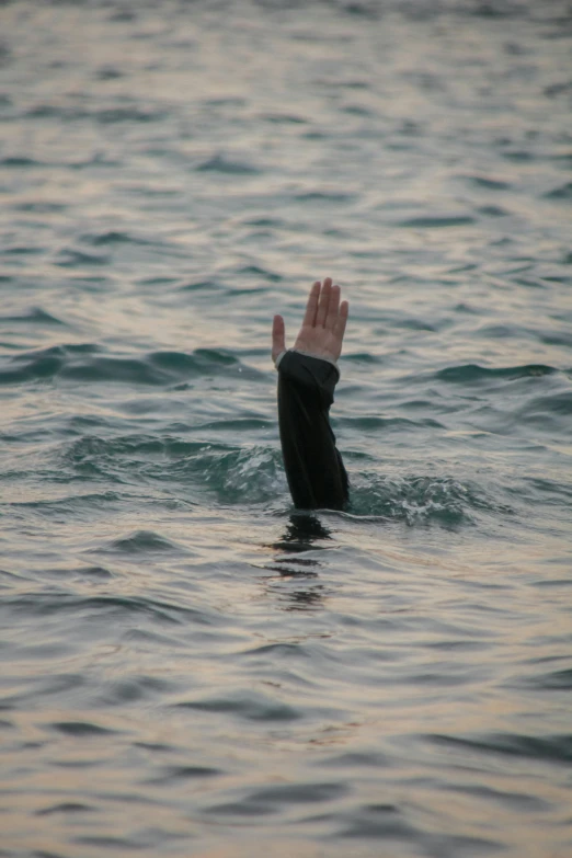 someone in the ocean making an gesture with their hand