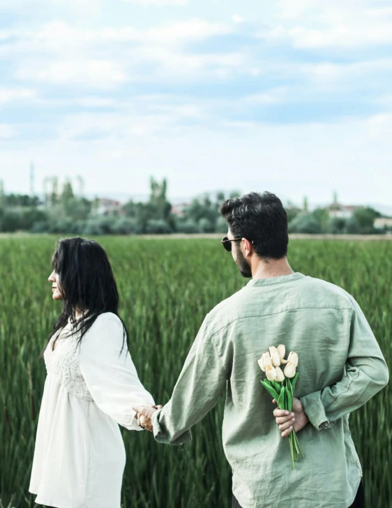 man and woman holding hands walking through field with tall grass
