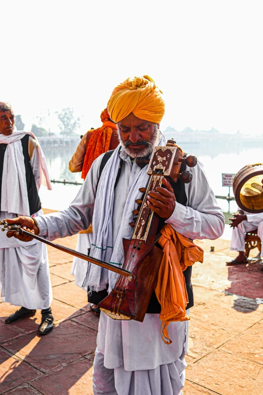 a man in indian attire holding a bow on the side of the lake