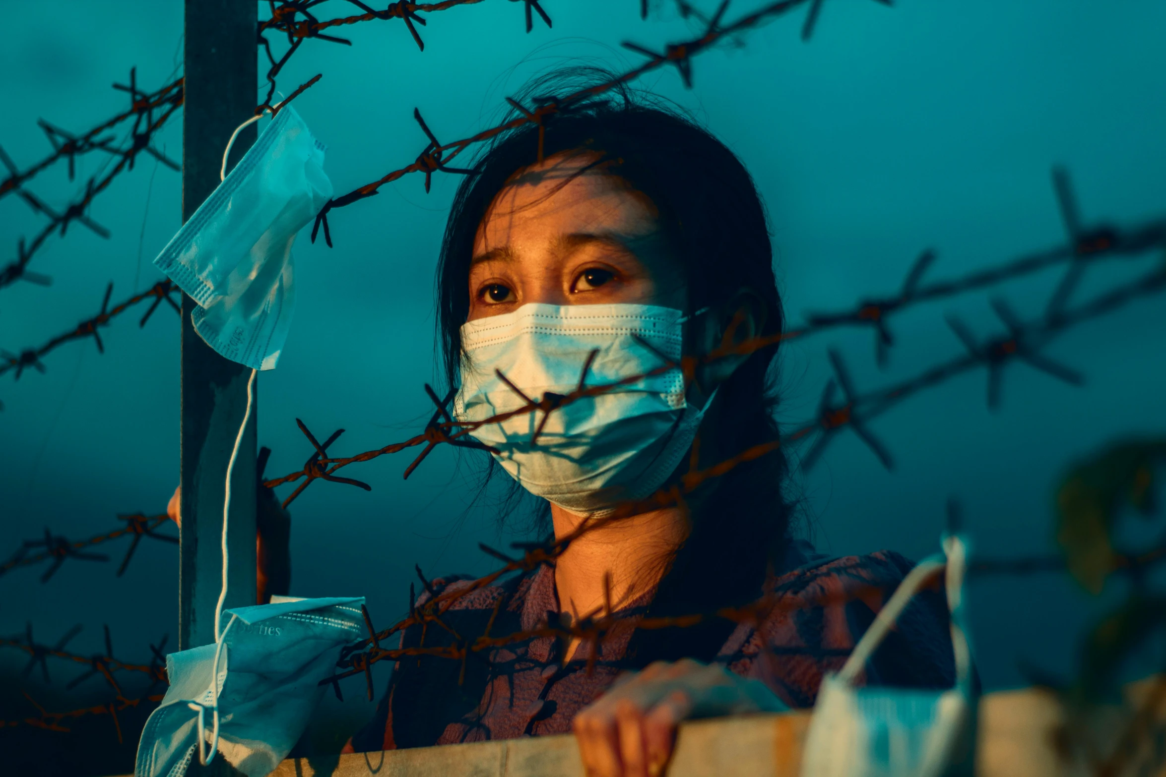 a woman in a face mask standing behind a wall with barbed wire