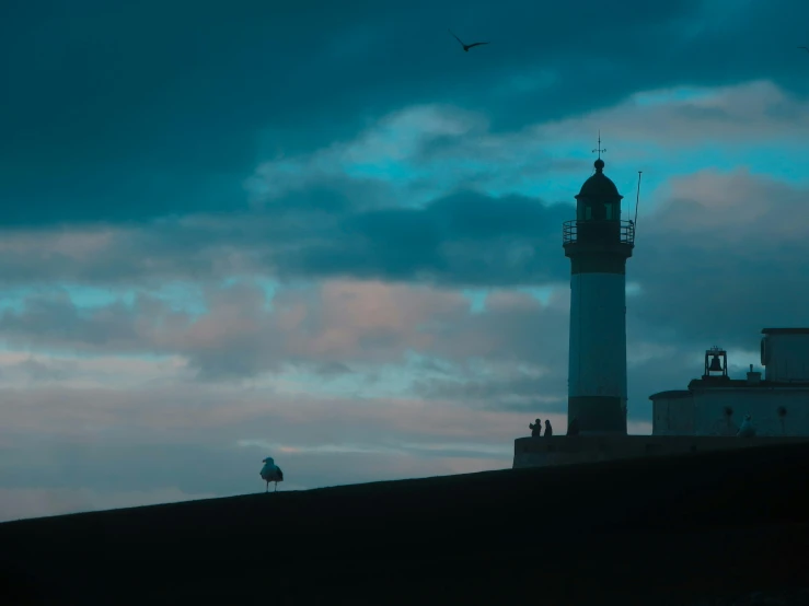 a lighthouse and a cloudy sky on top of the hill