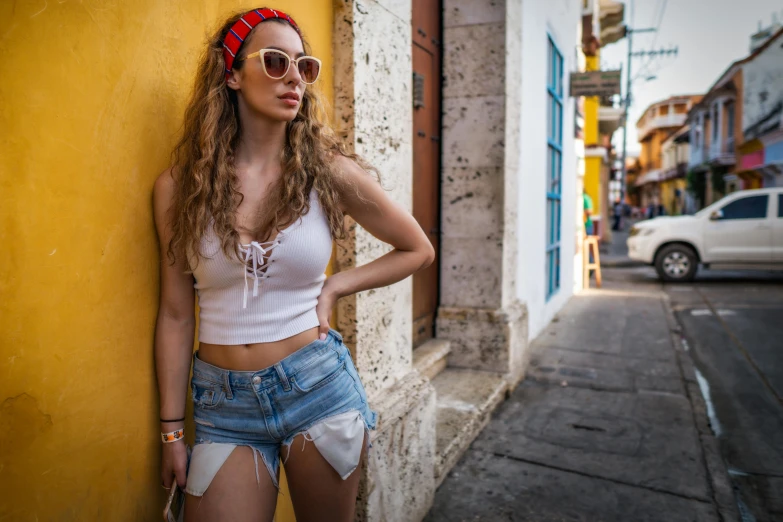 a young woman in ripped jeans leaning on a yellow wall