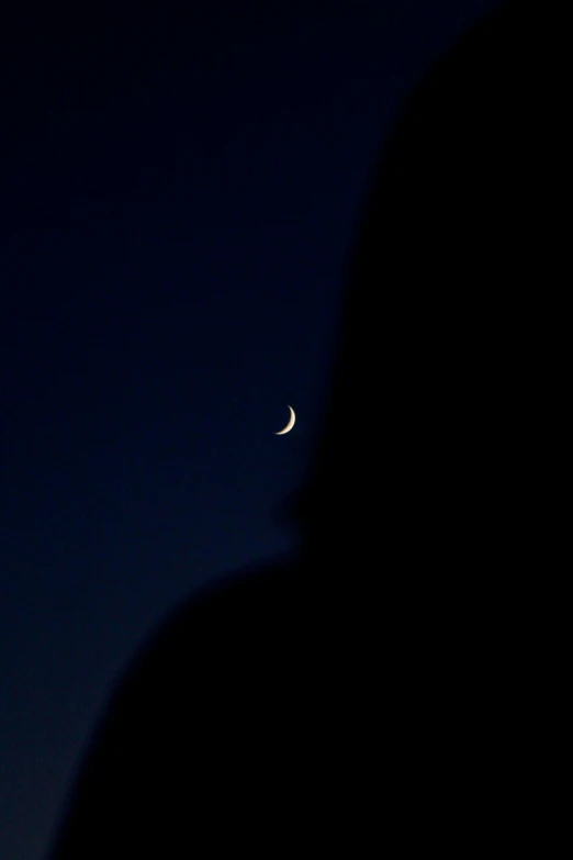 a crescent is seen in the dark sky behind a silhouetted person