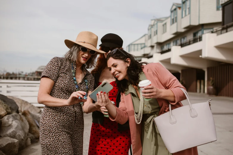 three woman in dresses posing for a picture while holding cell phones