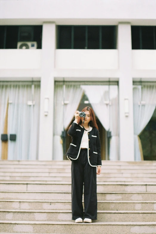 a woman stands outside with a camera in front of some stairs