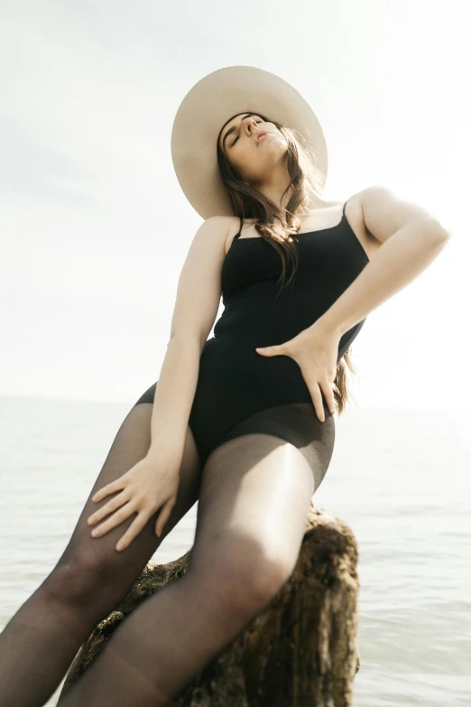 a woman wearing a swimsuit and a hat standing on a rock