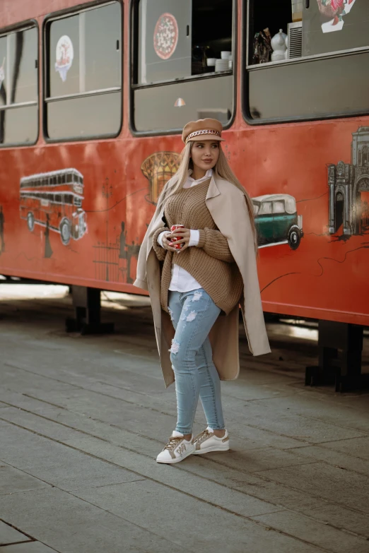 a girl in white sneakers and a trench coat stands by a bus