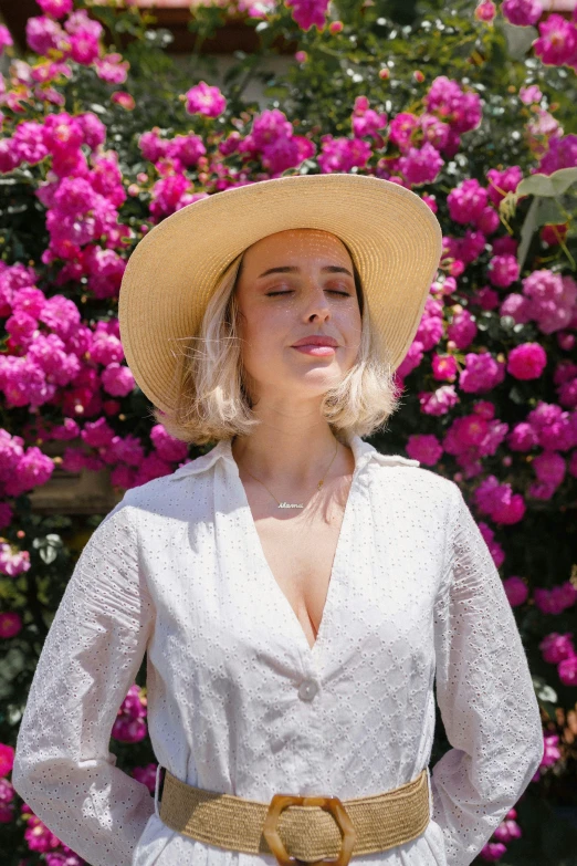 a woman in white dress and straw hat, standing in front of pink flowers